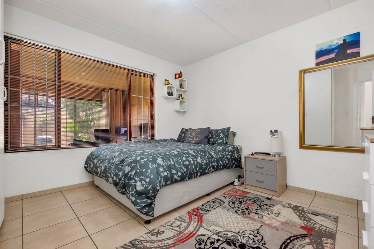 A well-lit bedroom featuring neutral tiled flooring and a large window with venetian blinds, offering a clean and functional living space.