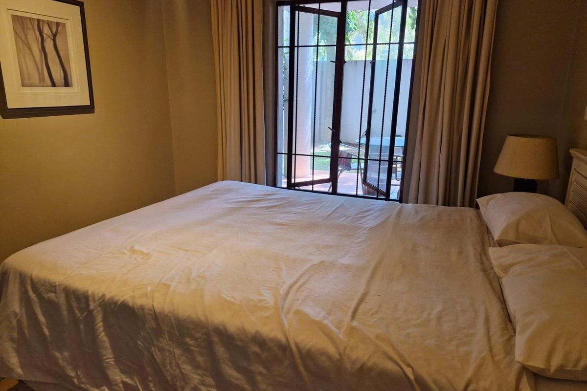 A comfortable bedroom featuring neutral wall tones, built-in curtain tracks, and a glass-paneled door providing direct access to an outdoor patio area.