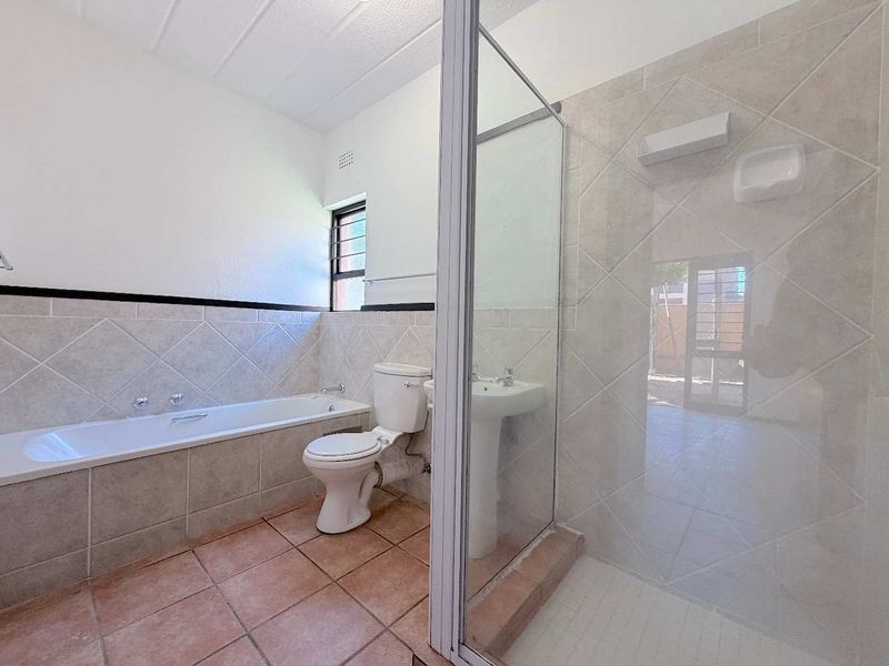 A functional bathroom featuring a built-in bathtub, pedestal sink, toilet, and a separate glass-enclosed shower with neutral ceramic tiling.