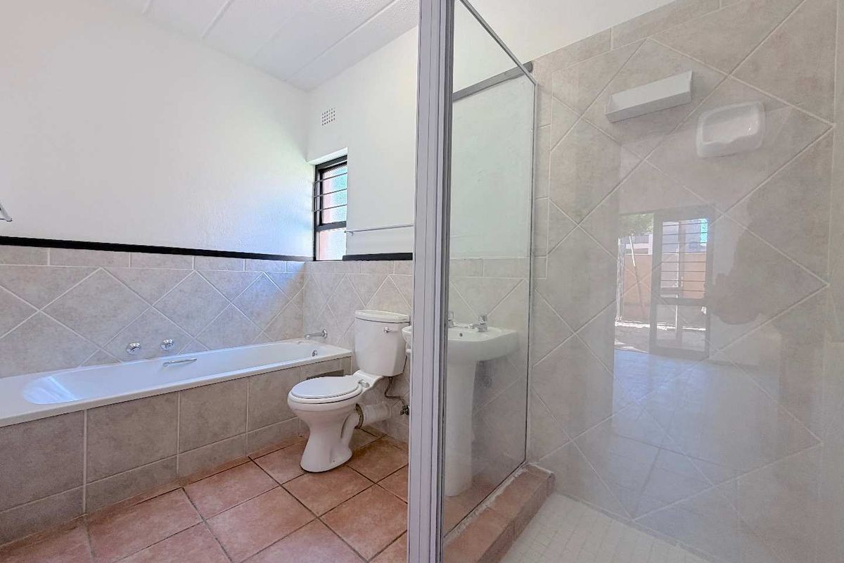 A functional bathroom featuring a built-in bathtub, pedestal sink, toilet, and a separate glass-enclosed shower with neutral ceramic tiling.