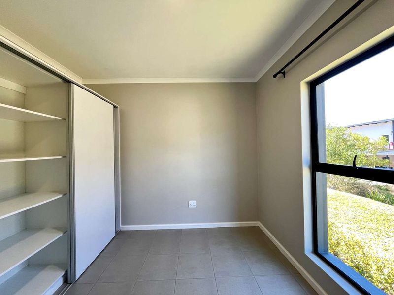 A bright, empty bedroom featuring neutral tiled flooring, a built-in wardrobe with sliding doors, and a large window providing natural light.