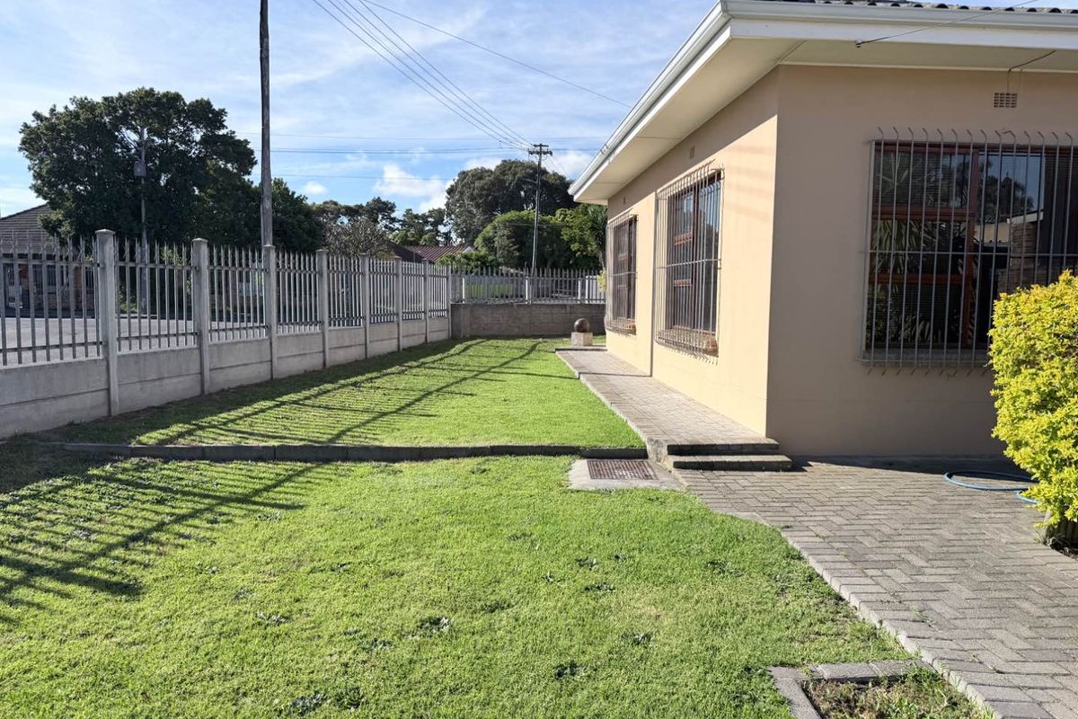 A well-maintained rear garden featuring a paved walkway, manicured lawn, and secure perimeter fencing with a concrete wall.