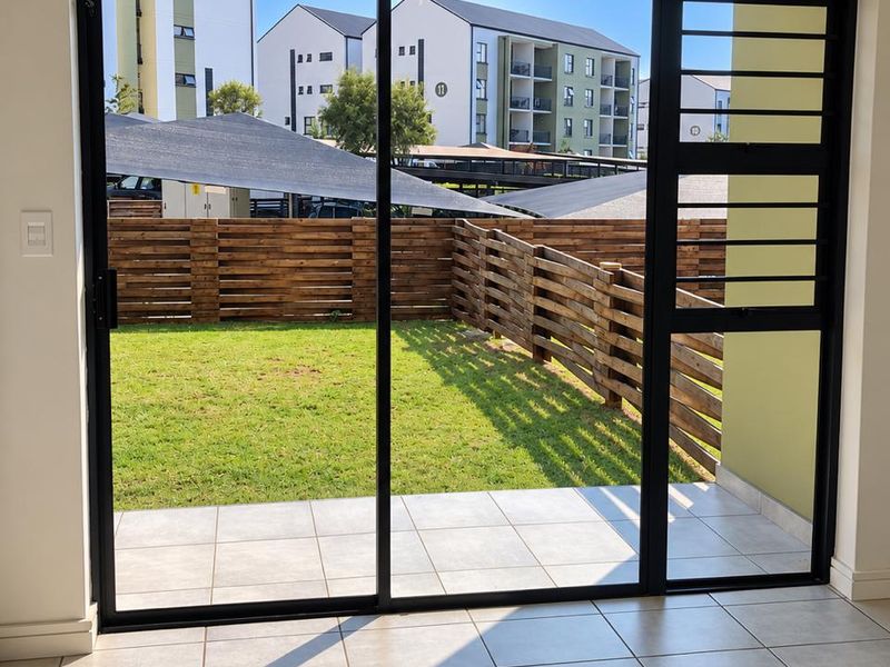Bright living area featuring large sliding glass doors with security gate, opening onto a private tiled patio and garden space.