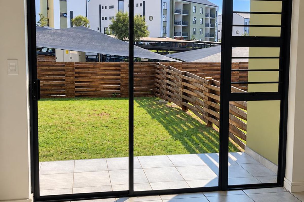 Bright living area featuring large sliding glass doors with security gate, opening onto a private tiled patio and garden space.