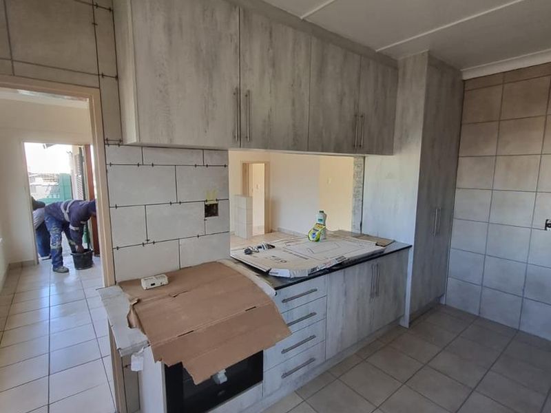 A kitchen currently under renovation featuring new cabinetry, tiled walls, and flooring, awaiting final finishes and completion of the installation.