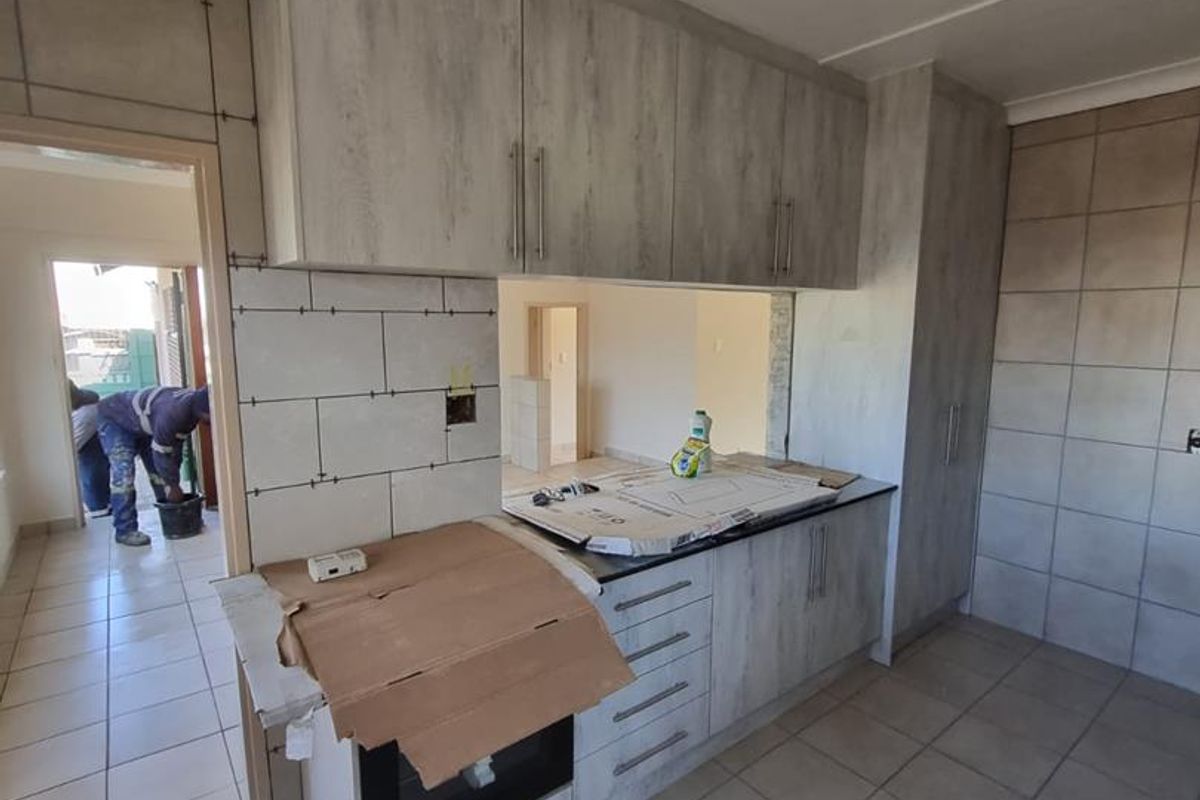 A kitchen currently under renovation featuring new cabinetry, tiled walls, and flooring, awaiting final finishes and completion of the installation.