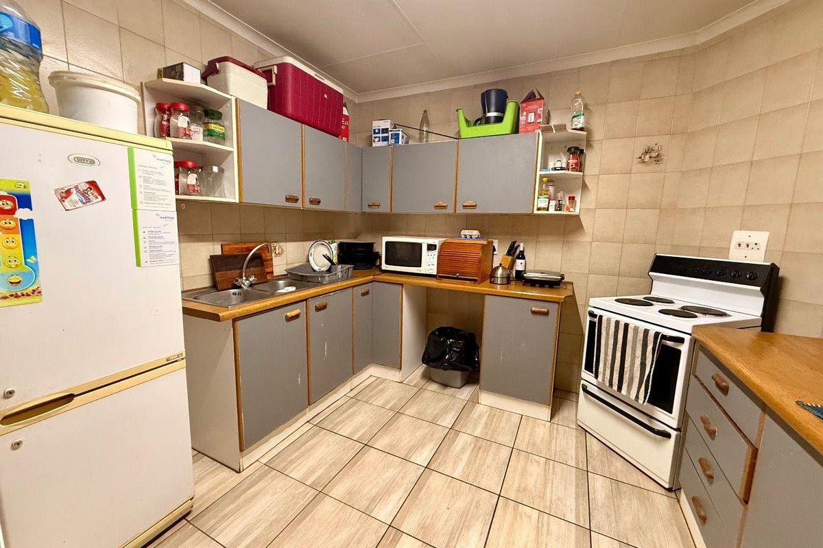 A functional kitchen featuring grey cabinetry, wood-look laminate countertops, tiled walls, and floor tiles, equipped with a freestanding stove and double sink.
