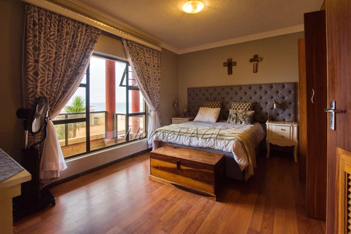 A well-lit bedroom featuring warm wood flooring, crown molding, and a large window providing natural light and access to an outdoor balcony area.
