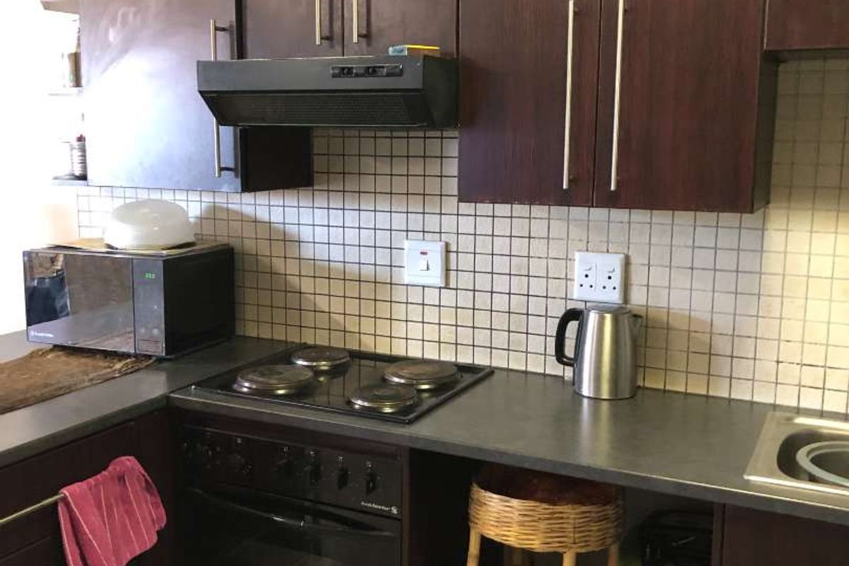 A functional kitchen featuring dark wood cabinetry, a built-in electric oven and hob, extractor fan, and tiled splashback.