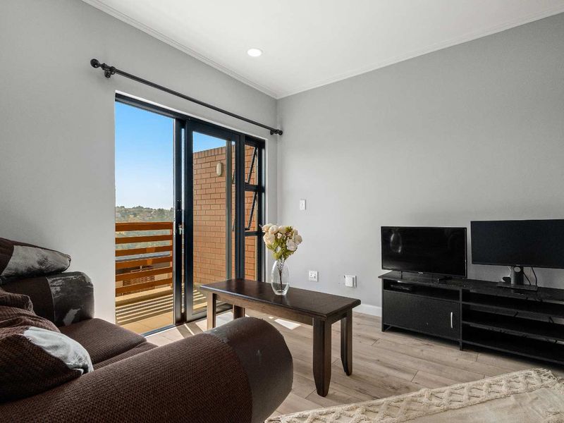 A bright living room featuring modern laminate flooring, neutral walls, and a sliding glass door providing access to an outdoor balcony area.