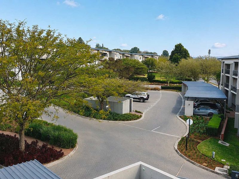 Elevated view overlooking the apartment complex grounds, featuring paved driveways, covered parking structures, and well-maintained landscaped garden areas.