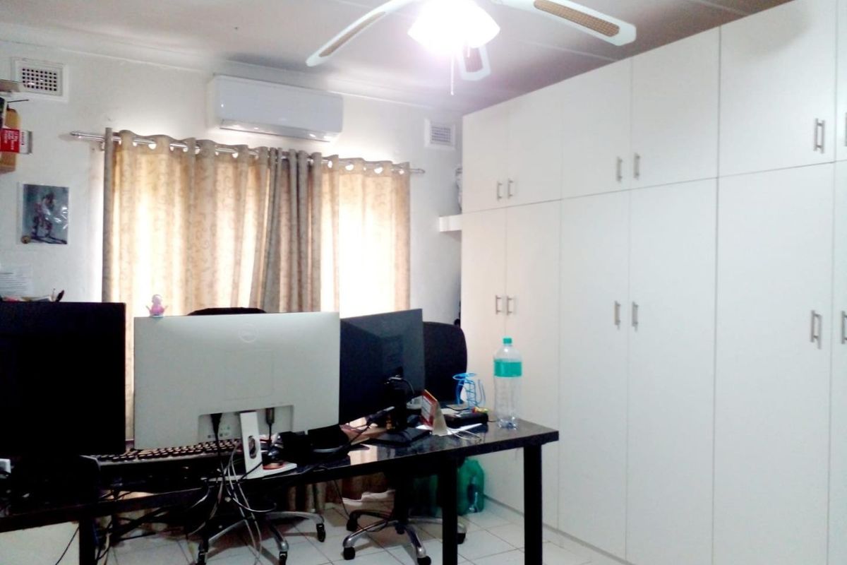 A bedroom featuring built-in cupboards, a ceiling fan, and a split-system air conditioner, currently utilized as a home office space.