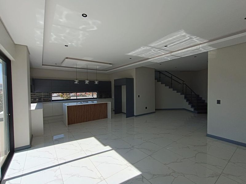 Spacious open-plan living area featuring a modern kitchen with a central island, sleek cabinetry, and a contemporary staircase with glass balustrades.