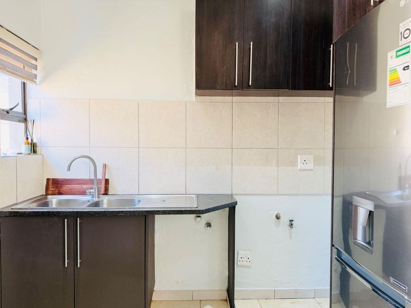 A functional kitchen area featuring dark wood cabinetry, granite countertops, a stainless steel double sink, and tiled backsplash with dedicated appliance plumbing connections.