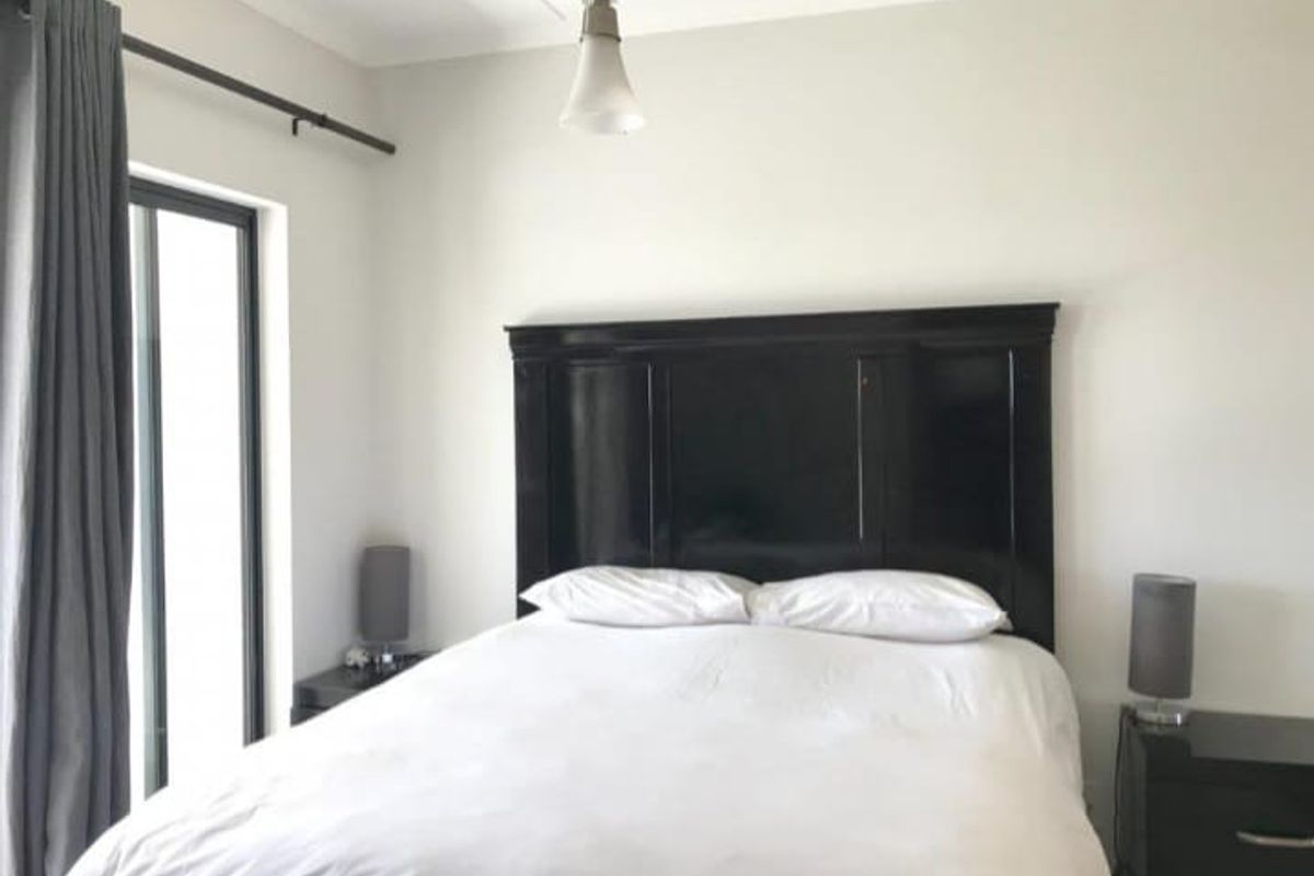 A well-maintained bedroom featuring neutral walls, a pendant light fixture, and a sliding glass door providing natural light.