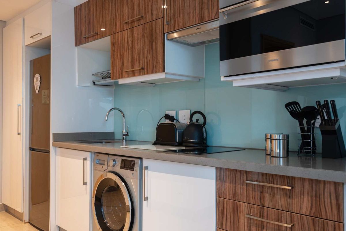 Modern kitchen featuring wood-grain and white cabinetry, stone countertops, glass splashback, integrated washing machine, and built-in microwave.