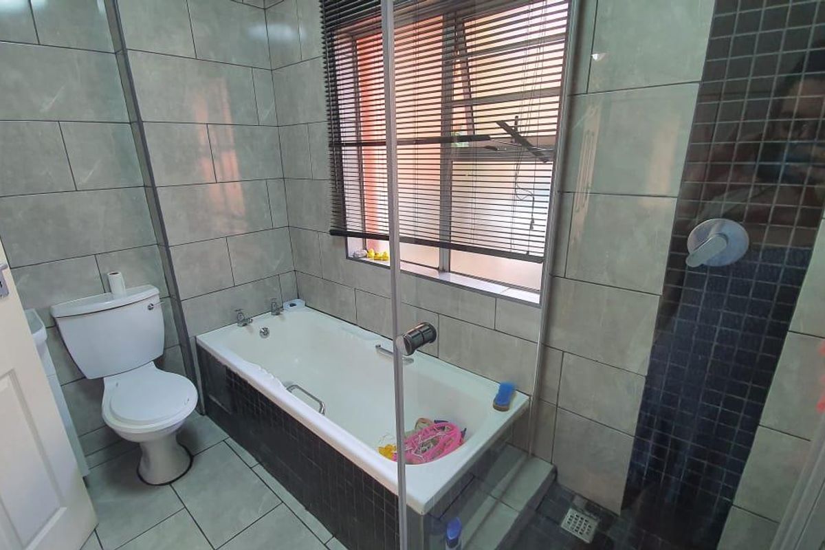 A modern bathroom featuring a tiled bathtub, a separate glass-enclosed shower, and a white toilet, finished with neutral wall and floor tiles.
