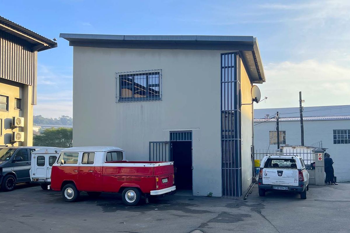 Exterior view of a commercial office building featuring security bars on windows and doors with an adjacent paved parking area.