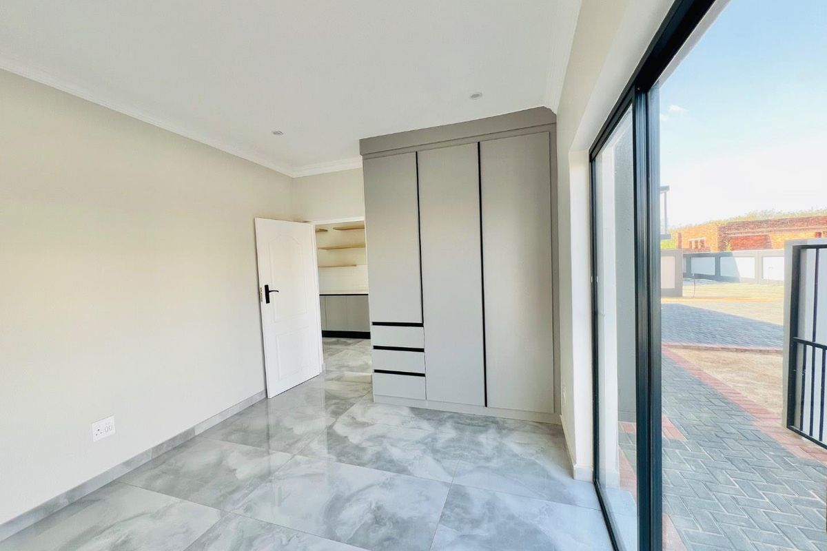 A bright, modern bedroom featuring large-format grey tiled flooring, built-in cupboards, and a sliding glass door providing access to the exterior.