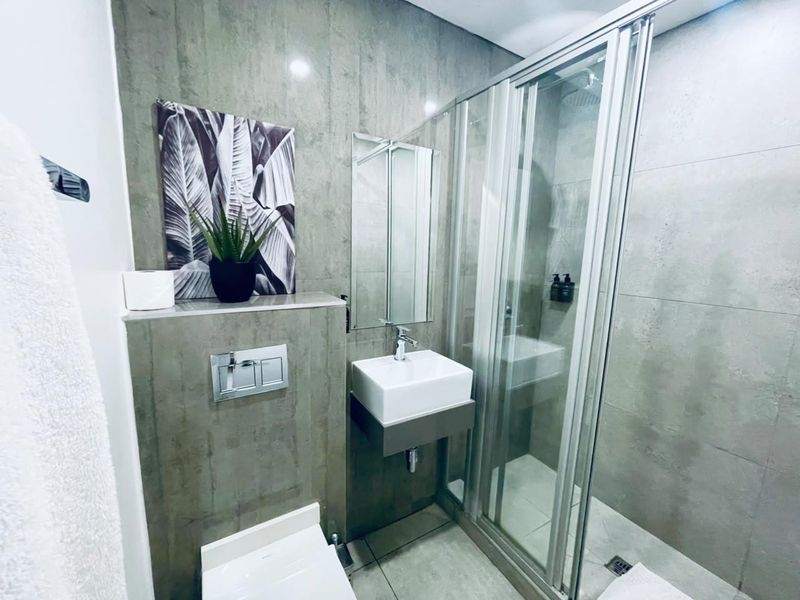 Modern bathroom featuring a wall-mounted vanity, concealed cistern toilet, and a glass-enclosed shower with contemporary grey tiling throughout.