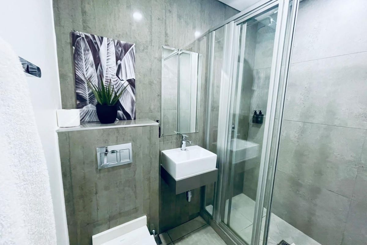 Modern bathroom featuring a wall-mounted vanity, concealed cistern toilet, and a glass-enclosed shower with contemporary grey tiling throughout.