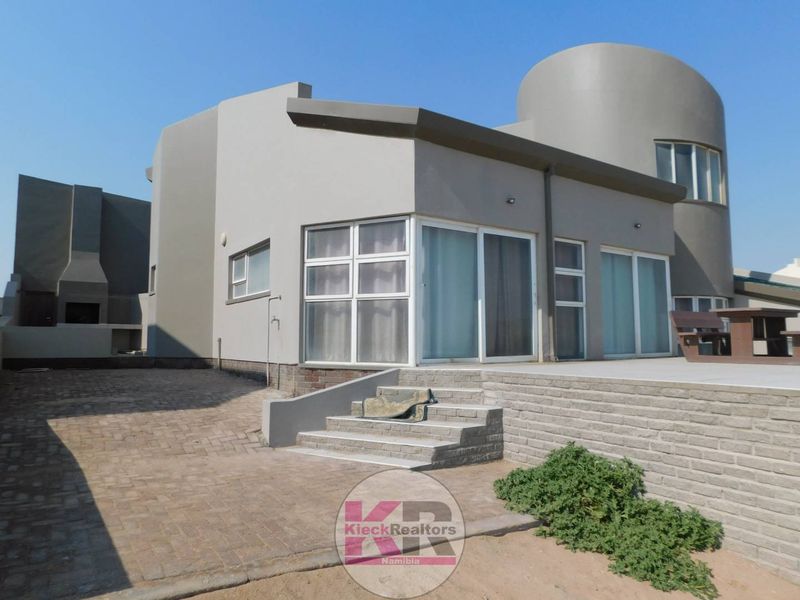 Rear view of a modern house featuring a paved driveway, concrete patio, outdoor fireplace, and large sliding glass doors leading into the home.