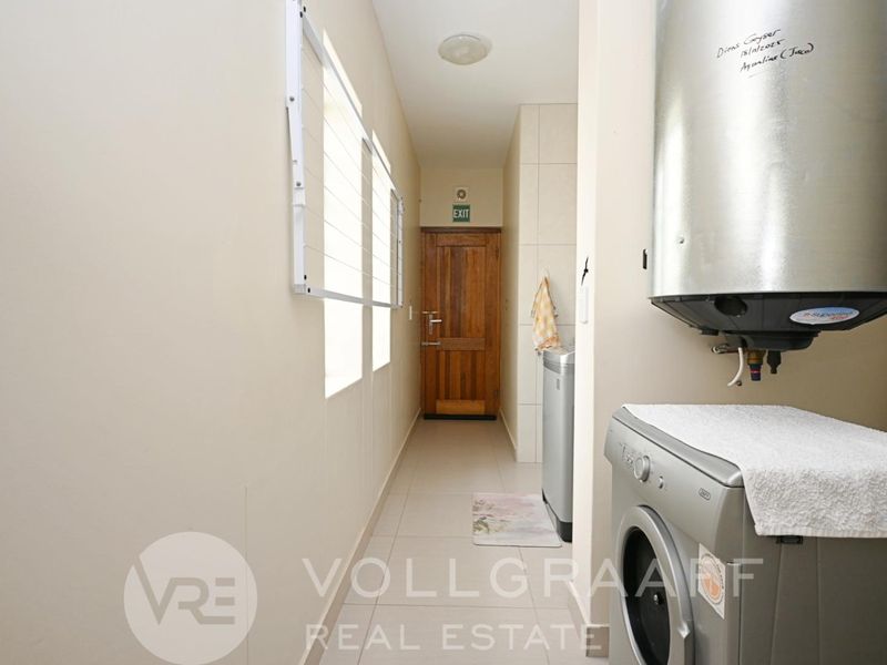A functional laundry area featuring tiled flooring, a wall-mounted drying rack, and an electric water geyser.