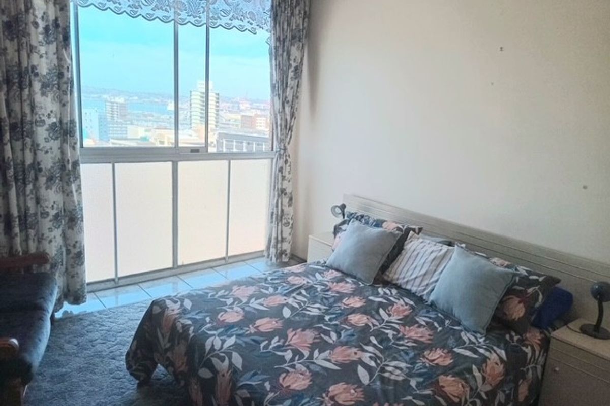 A bedroom featuring a large floor-to-ceiling window with expansive city views, built-in headboard, and tiled flooring.