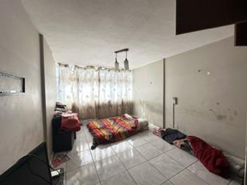 A bedroom featuring tiled flooring and a pendant light fixture, currently requiring cosmetic attention to the wall surfaces.