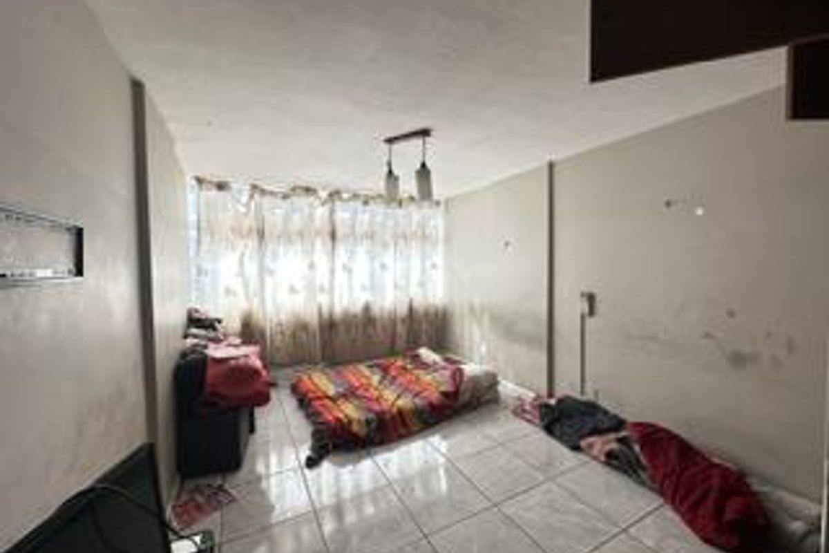 A bedroom featuring tiled flooring and a pendant light fixture, currently requiring cosmetic attention to the wall surfaces.