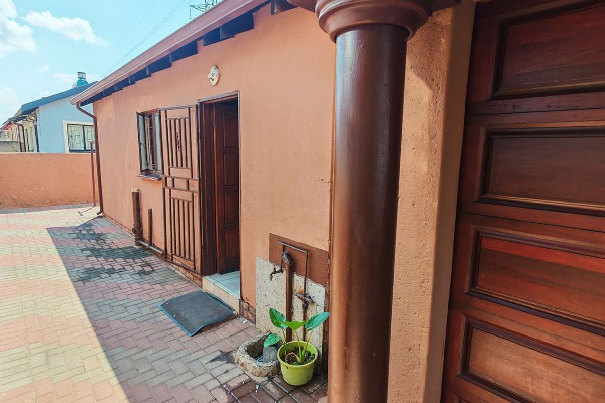 Rear exterior view featuring a paved patio area, timber door with security gate, and an external water tap against a plastered wall.