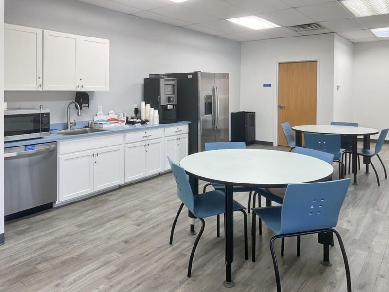 A functional office breakroom featuring white cabinetry, stainless steel appliances, a sink, and durable laminate flooring with a drop ceiling.