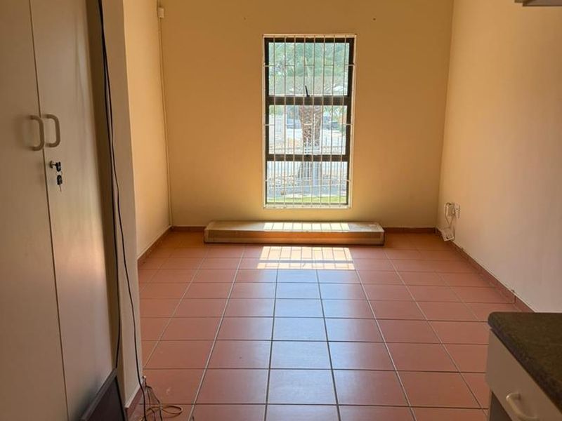An empty living area featuring tiled flooring, built-in cupboards, and a window fitted with security bars.