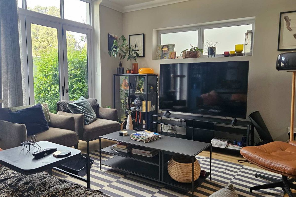A bright living room featuring laminate flooring, coving, and large french doors with transom windows providing ample natural light and garden access.