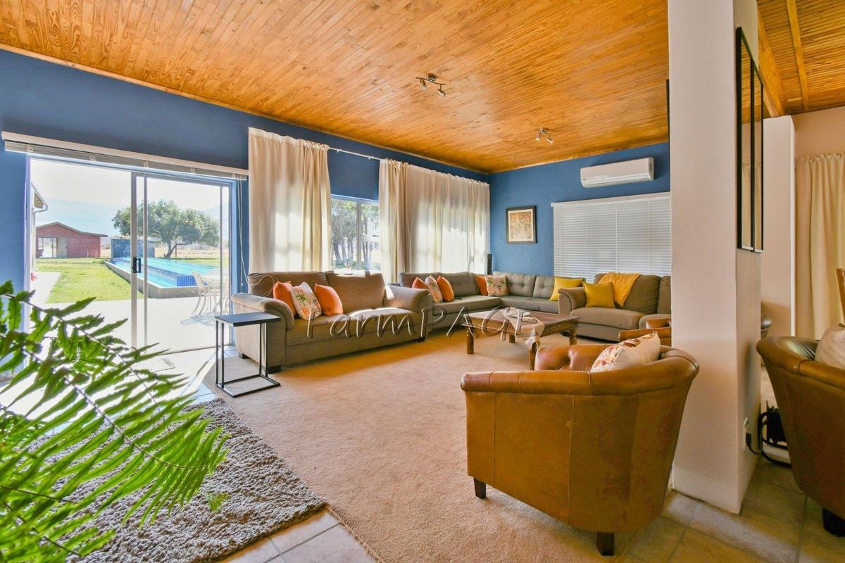 Spacious living room featuring a high timber-clad ceiling, large sliding glass doors leading to the pool area, and a wall-mounted air conditioning unit.