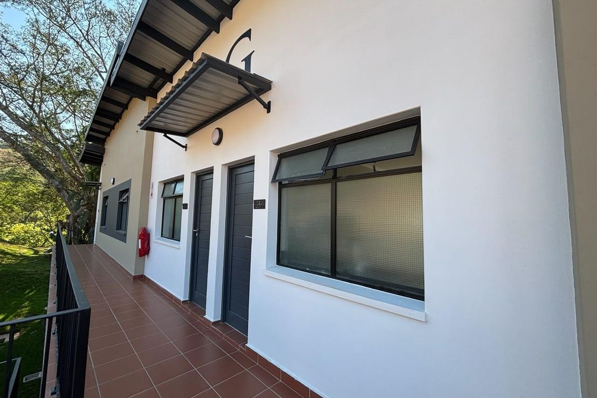 Exterior view of an apartment walkway featuring tiled flooring, metal railings, and modern dark-framed doors and windows with protective awnings.