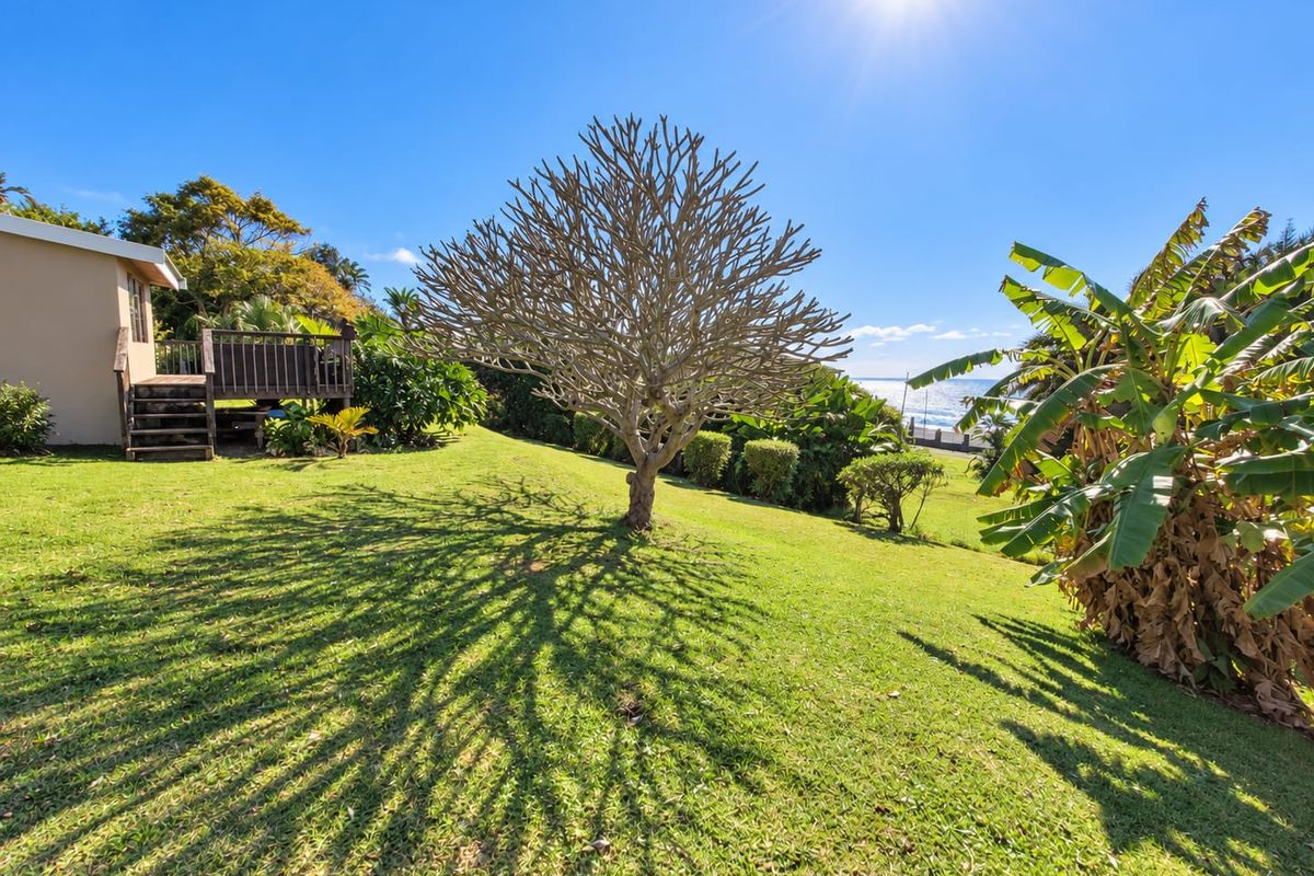 A spacious rear garden featuring a well-maintained lawn, mature trees, and a raised wooden deck attached to the side of the house.