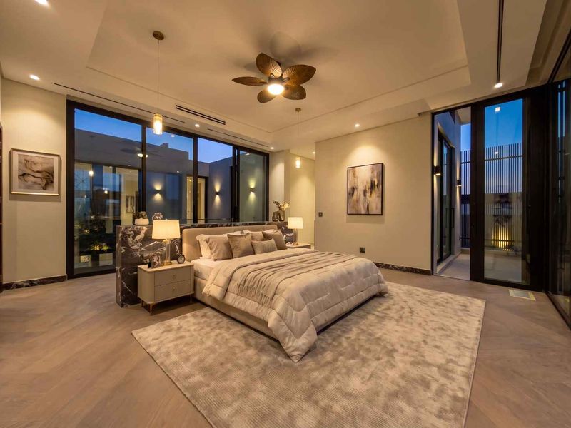 A luxurious, modern bedroom featuring herringbone timber flooring, a marble feature wall, and expansive floor-to-ceiling glass doors opening to an outdoor area.