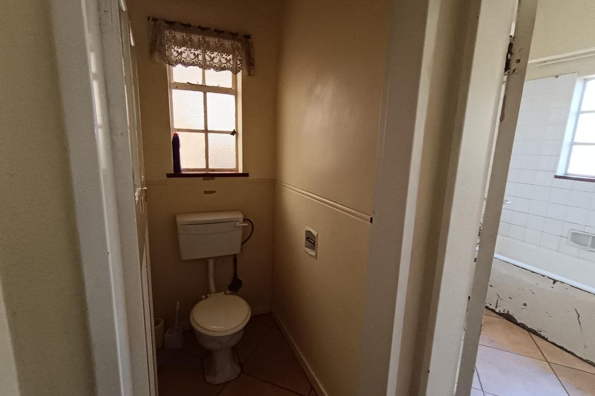 A small, dated bathroom featuring a separate toilet area and a bathtub with visible wear on the base.