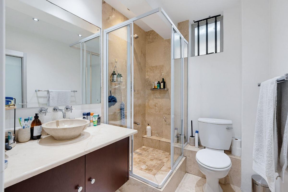 A well-maintained bathroom featuring a stone vessel sink, vanity cabinet, glass-enclosed shower with stone tiling, and a modern toilet.