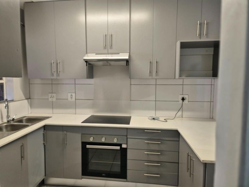 Modern kitchen featuring grey cabinetry, stone countertops, built-in oven, electric hob, extractor fan, and a double sink with a tiled backsplash.