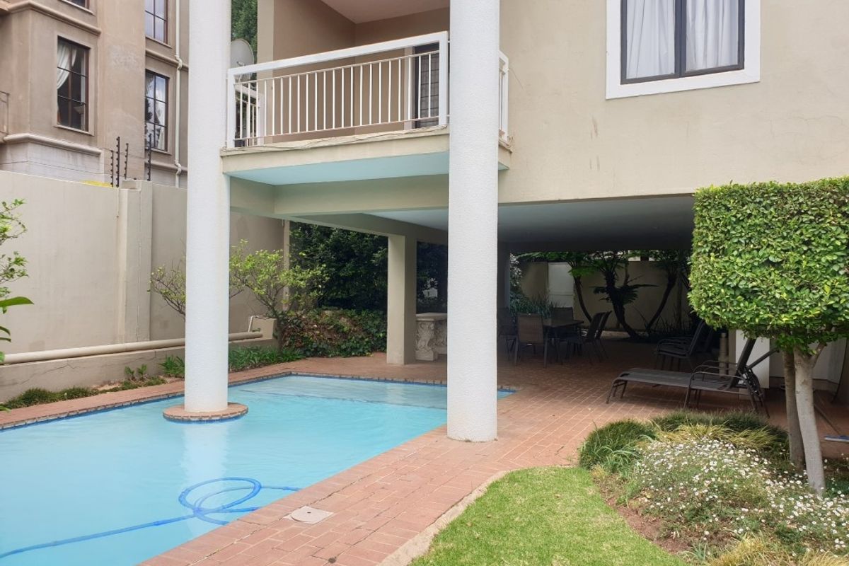 Rear view of the apartment featuring a swimming pool, covered patio area, and a balcony with white railings.