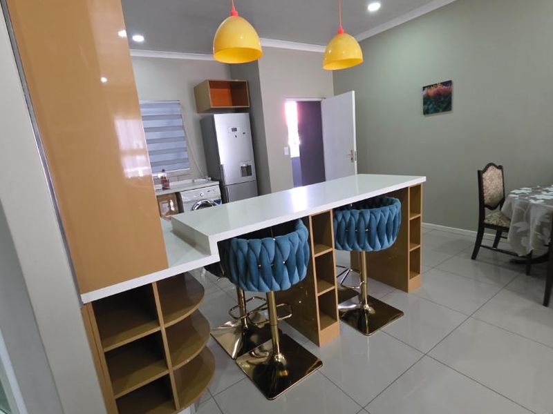 Open plan living area featuring a modern breakfast bar with integrated storage, tiled flooring, and contemporary pendant lighting.