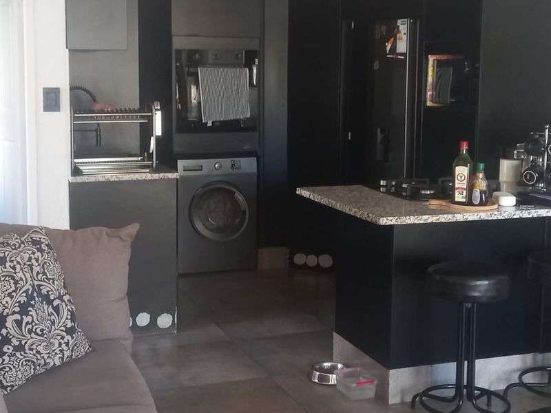 Open plan living and kitchen area featuring modern dark cabinetry, granite countertops, a kitchen island, and integrated laundry facilities.