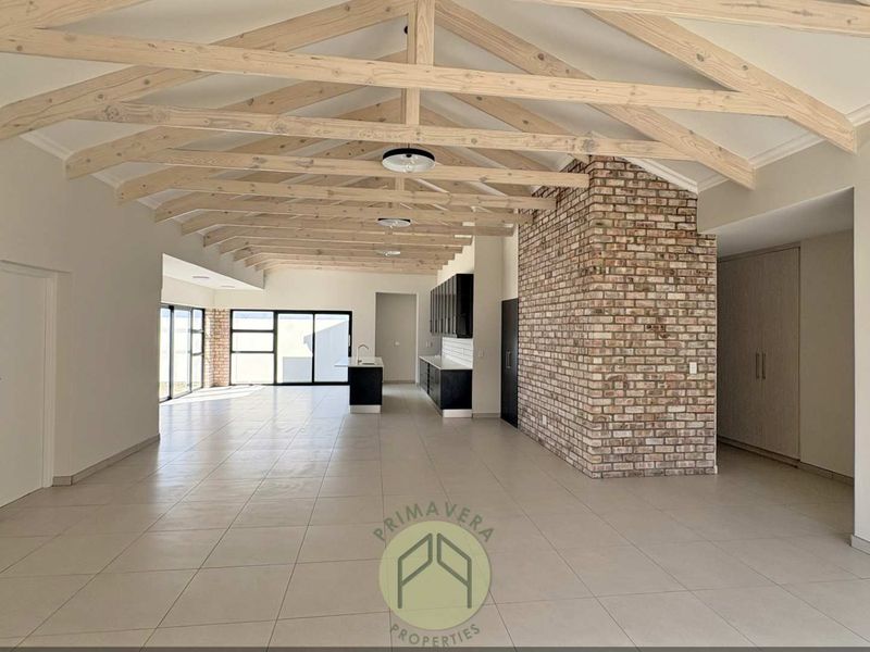 Spacious open-plan living area featuring exposed timber trusses, a striking brick feature wall, modern kitchen cabinetry, and large sliding doors leading outdoors.