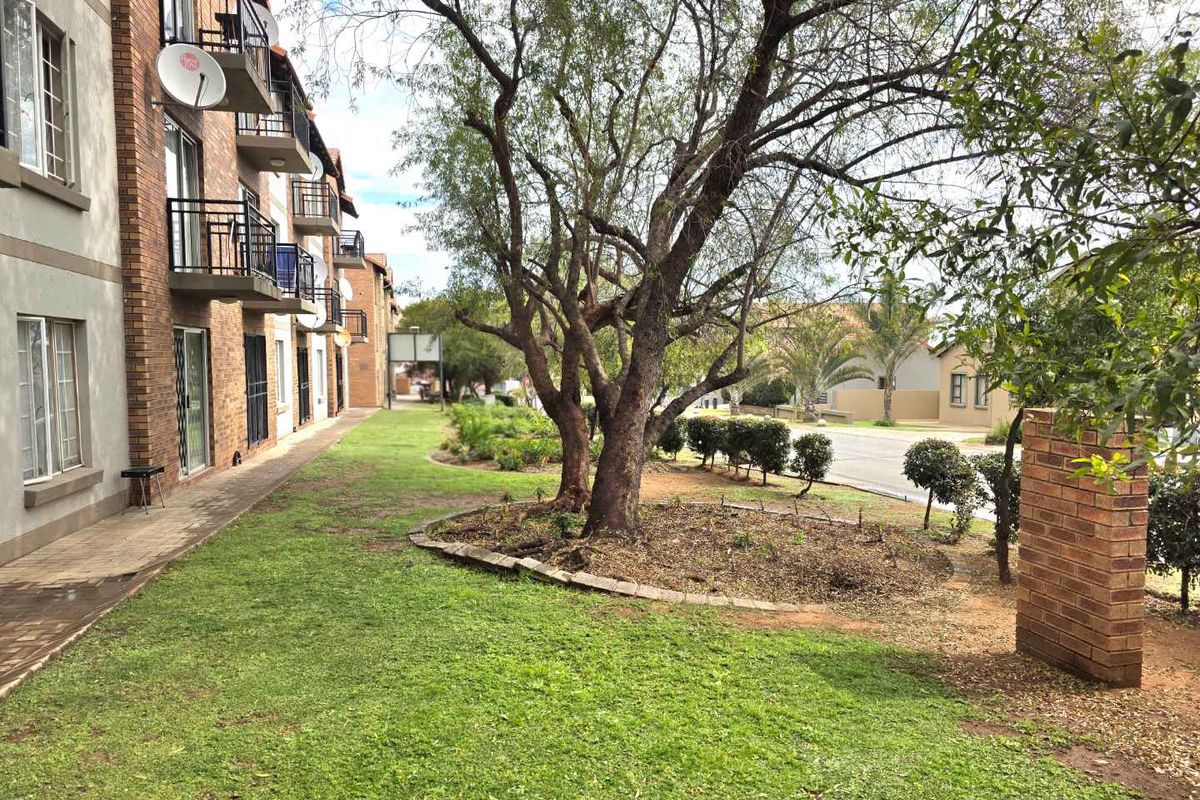 A view of the apartment complex exterior featuring a landscaped garden, paved walkways, and private balconies on the building facade.