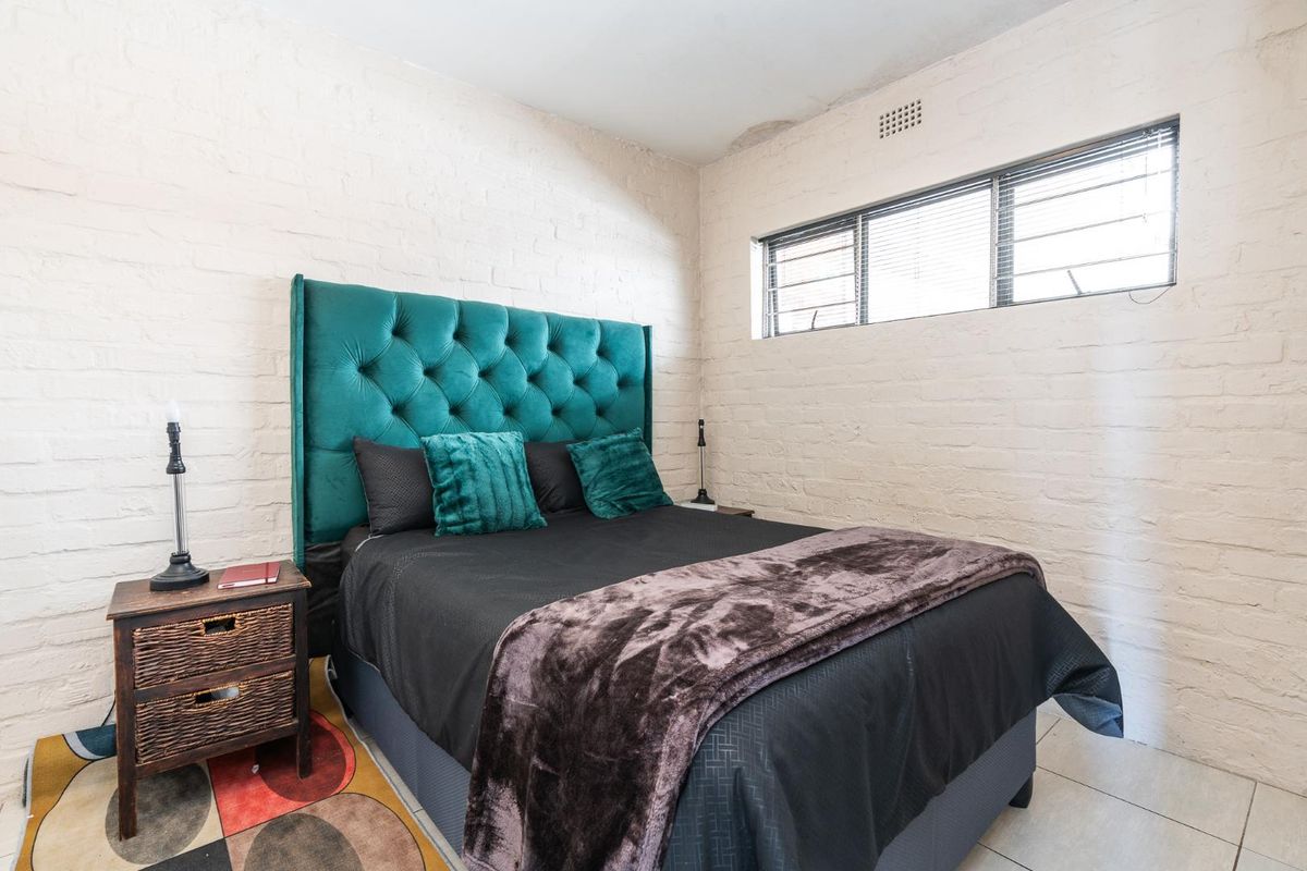 A bedroom featuring exposed brick walls, tiled flooring, and a high-set window with aluminium frames.