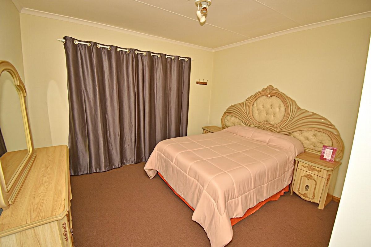A standard bedroom featuring neutral wall paint, carpeted flooring, and a window covered by curtains.