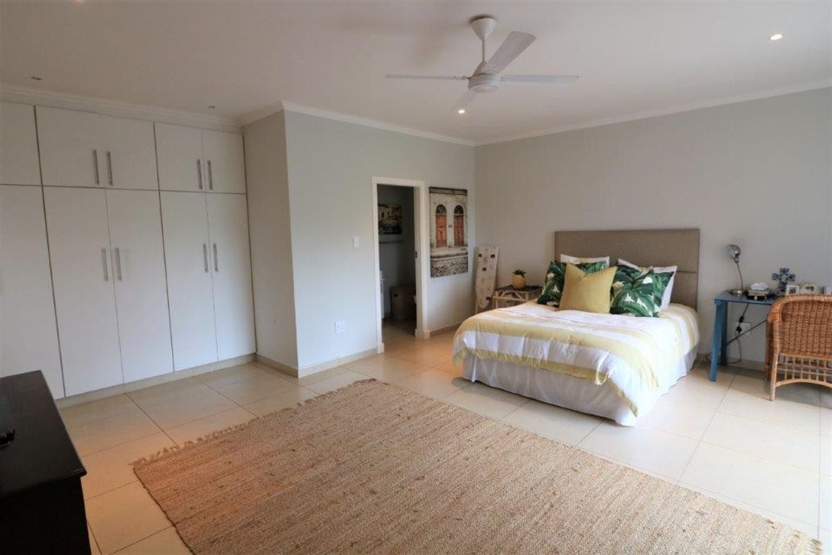 Spacious bedroom featuring neutral tiled flooring, extensive built-in cabinetry, and a ceiling fan, with an adjoining en-suite or walk-in closet area.
