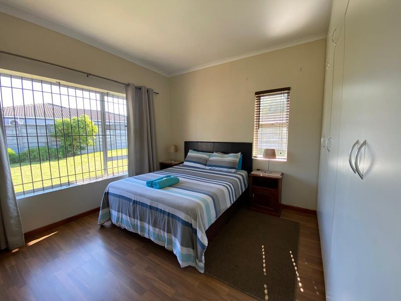 A functional bedroom featuring laminate flooring, built-in cupboards, and security bars on the windows, offering a clean and practical living space.